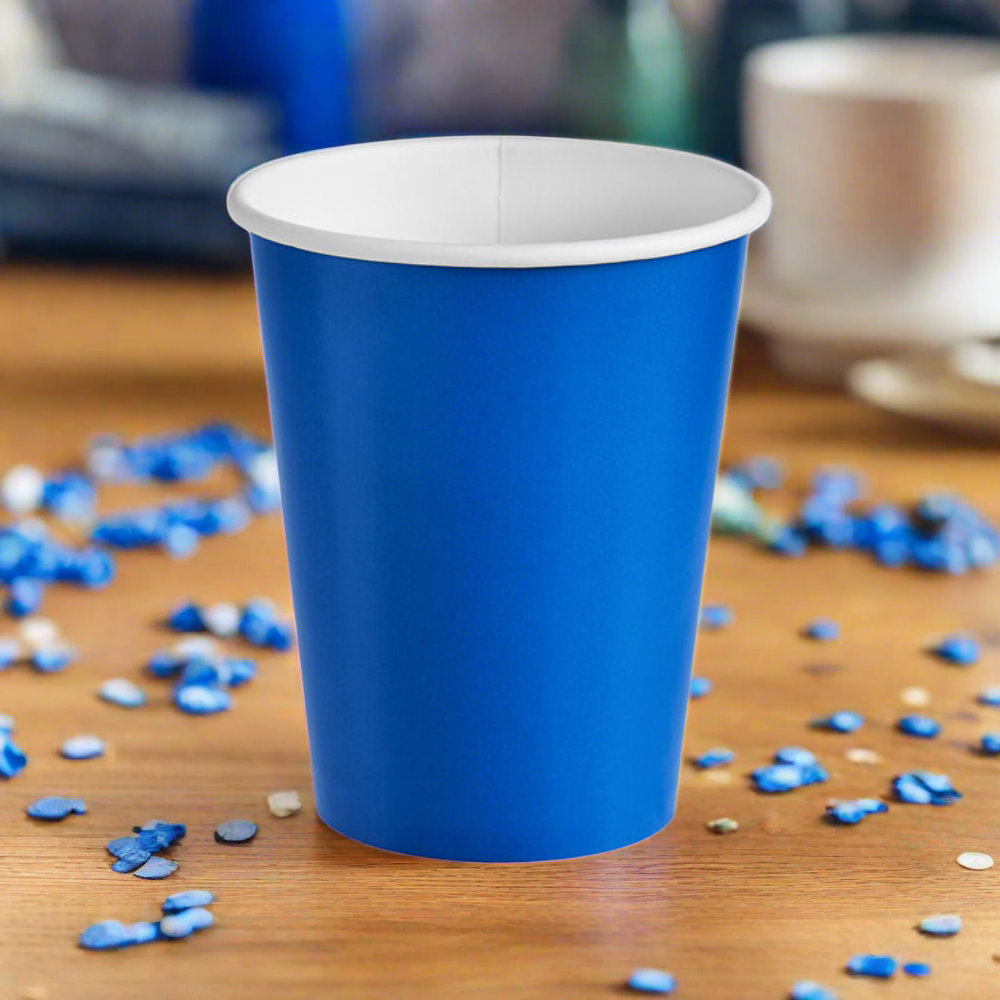 cobalt blue, 9 oz paper party cup for hot and cold drinks, sitting on wood table with blue confetti