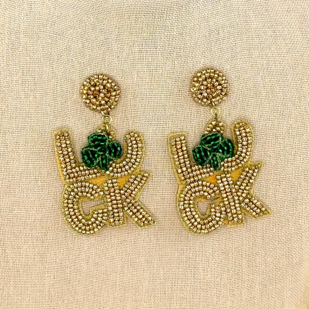 pair of gold, seed bead LUCK St. Patrick's Day dangle earrings with green clover on canvas background