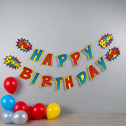 Large superhero happy birthday banner with bam, boom, smash, wham for superhero birthday party hanging on wall with balloons on floor